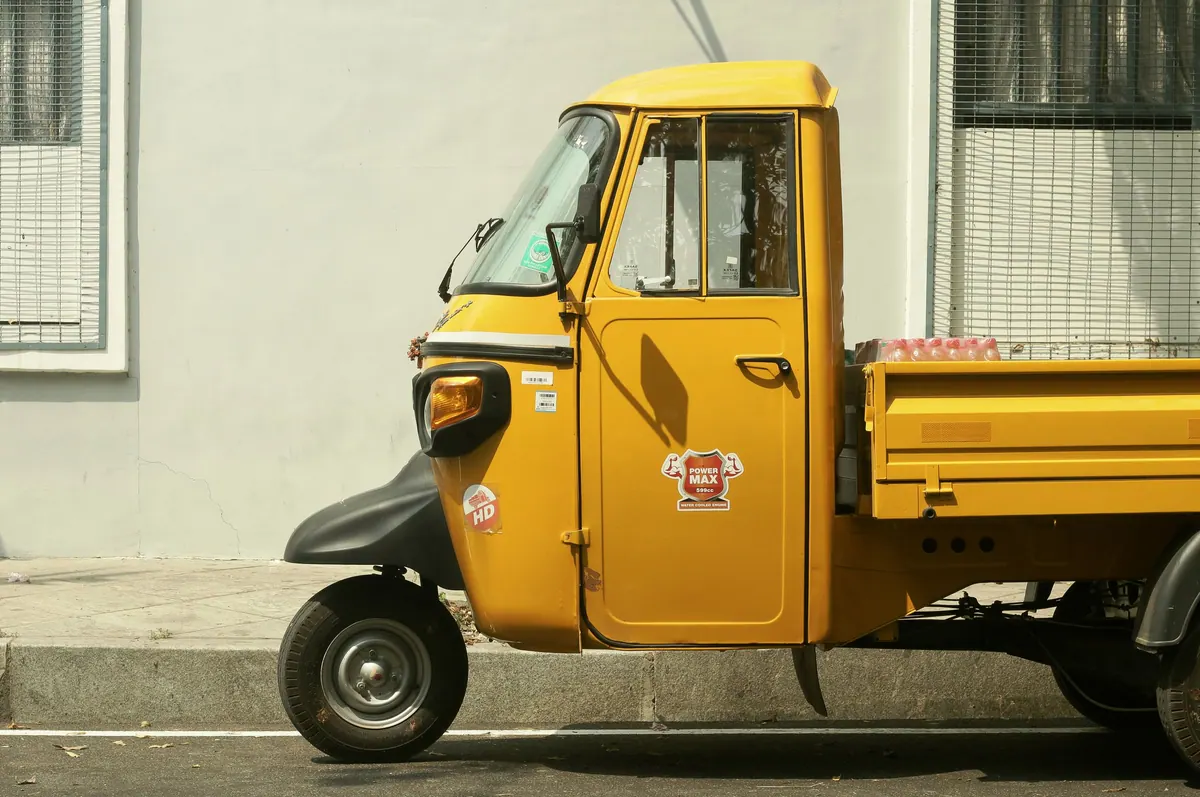 A yellow three-wheeled goods carrier parked on a street