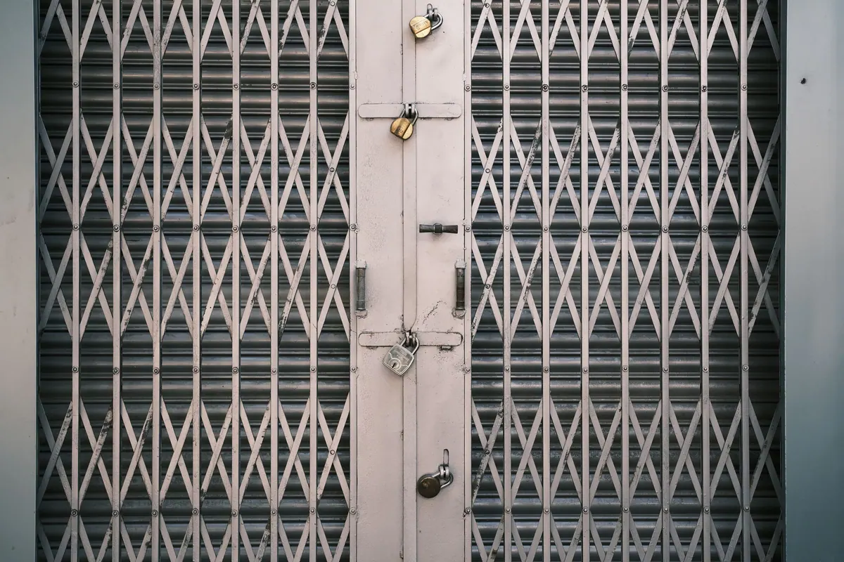 A collapsible steel shop gate held shut by four separate padlocks